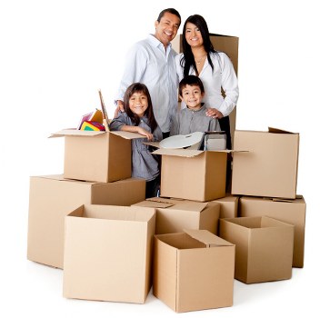 A family of four, consisting of a man, woman, and two children, standing inside a room filled with open cardboard moving boxes of various sizes, some stacked and others placed on the floor. The boxes are made of brown corrugated cardboard and contain household items such as a rolled-up rainbow-colored mat, a lamp, and packing paper. The family members are smiling and appear to be in the process of packing or unpacking during a house move. The background suggests an indoor environment with neutral lighting, emphasizing the presence of household belongings ready for relocation within Westminster or nearby areas. The scene captures a typical home environment associated with professional house removals provided by Westminster Man with Van services.