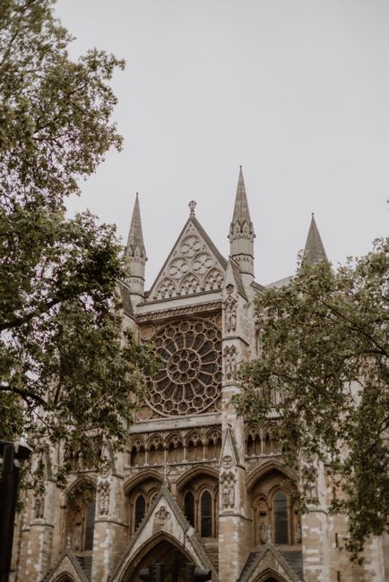 A detailed front view of Westminster Abbey showing its Gothic architecture with pointed arches, tall spires, and intricate stone carvings. The large rose window is prominently visible above the main e